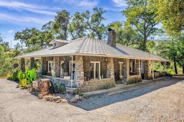 view of front of house featuring stone siding, covered porch, and a chimney