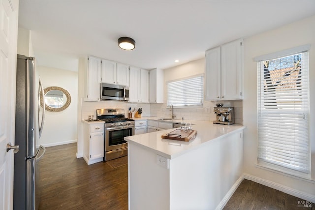 kitchen with white cabinetry, kitchen peninsula, stainless steel appliances, backsplash, and sink