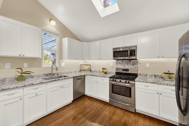 kitchen with sink, hardwood / wood-style flooring, lofted ceiling with skylight, stainless steel appliances, and white cabinets