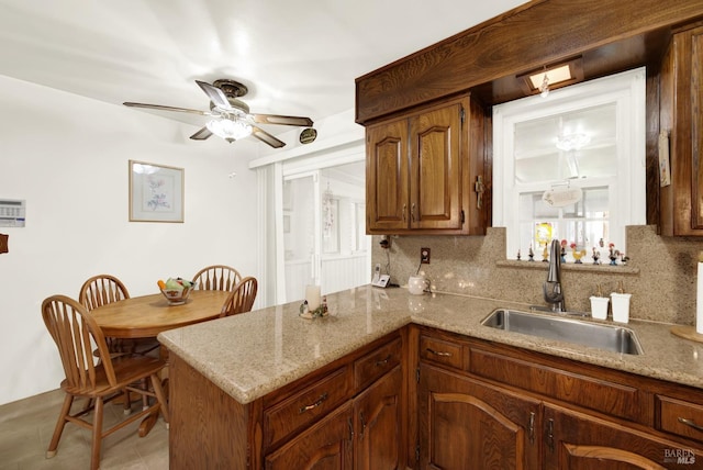 kitchen with light stone counters, backsplash, a sink, and a peninsula