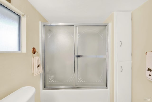 bathroom featuring toilet and bath / shower combo with glass door