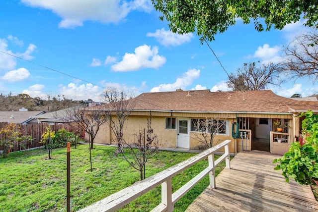 rear view of house with roof with shingles, a yard, fence, and stucco siding