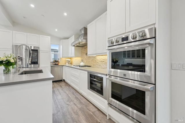 kitchen featuring appliances with stainless steel finishes, wall chimney exhaust hood, lofted ceiling, white cabinetry, and tasteful backsplash