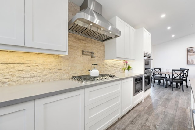 kitchen with tasteful backsplash, light hardwood / wood-style floors, white cabinetry, appliances with stainless steel finishes, and ventilation hood