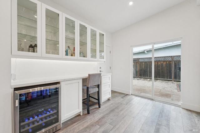 bar with white cabinets, beverage cooler, and light hardwood / wood-style flooring