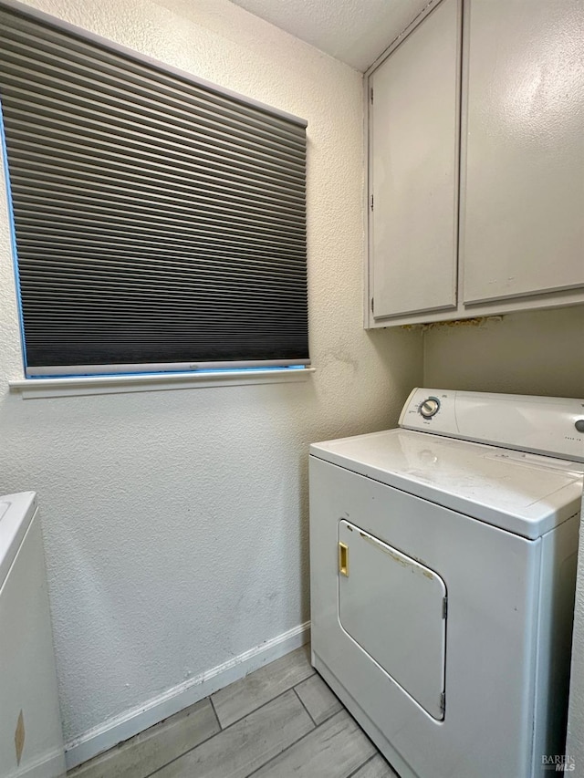 clothes washing area featuring washer and dryer, a textured ceiling, and cabinets