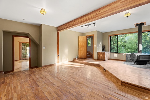living room with baseboards, a wood stove, wood finished floors, and beamed ceiling