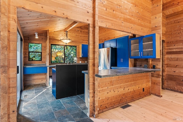 kitchen featuring lofted ceiling with beams, blue cabinets, freestanding refrigerator, glass insert cabinets, and wood walls