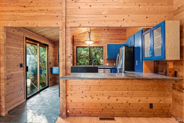 kitchen featuring wooden walls, kitchen peninsula, blue cabinetry, hanging light fixtures, and appliances with stainless steel finishes