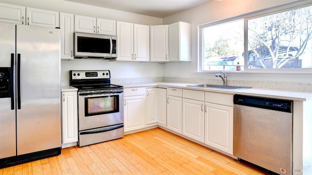 kitchen with stainless steel appliances, white cabinetry, sink, and light wood-type flooring