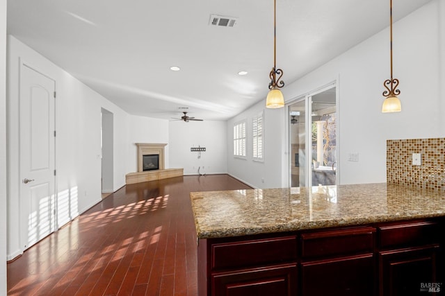 kitchen featuring ceiling fan, pendant lighting, light stone counters, and backsplash