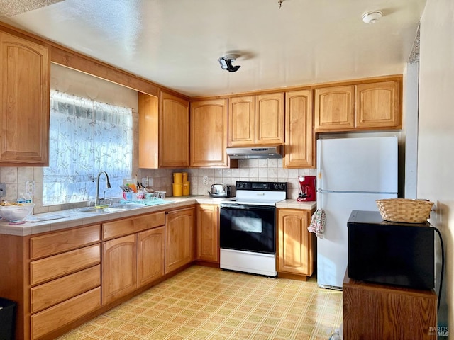 kitchen featuring under cabinet range hood, electric range, a sink, backsplash, and freestanding refrigerator