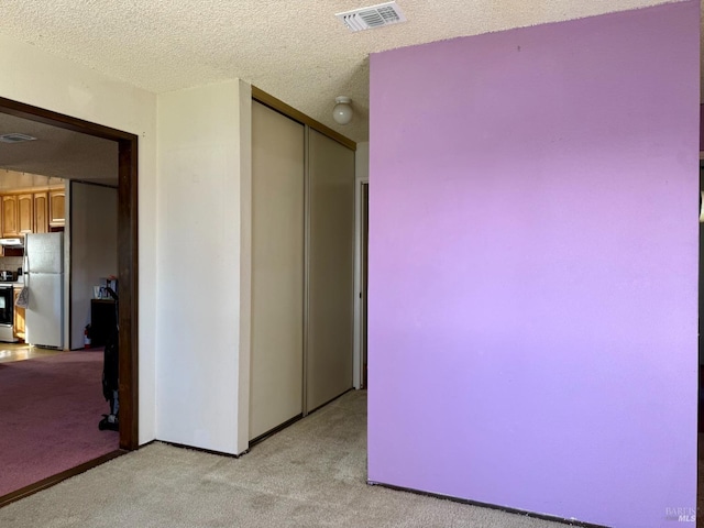 unfurnished bedroom featuring a closet, visible vents, freestanding refrigerator, light carpet, and a textured ceiling