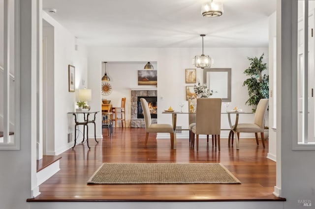 dining space with a notable chandelier, dark hardwood / wood-style flooring, and a stone fireplace