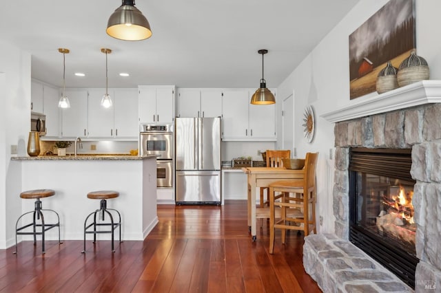 kitchen with kitchen peninsula, stone countertops, white cabinetry, a fireplace, and appliances with stainless steel finishes