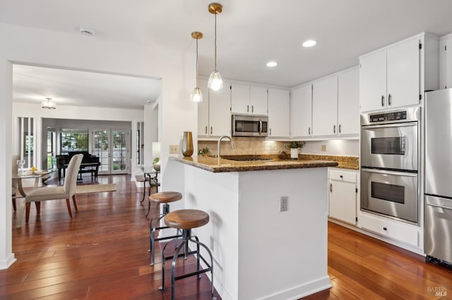 kitchen with white cabinets, a kitchen bar, dark stone countertops, tasteful backsplash, and appliances with stainless steel finishes