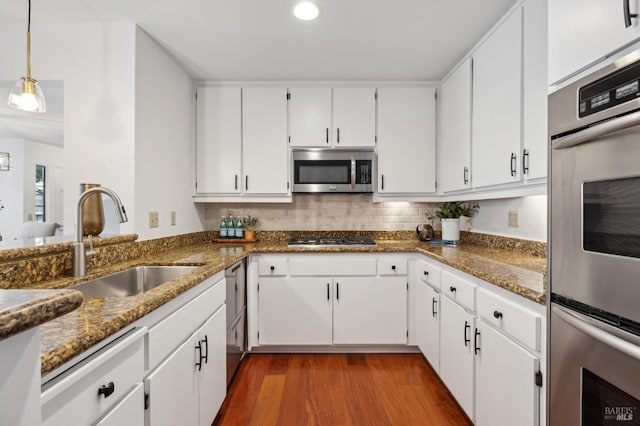 kitchen featuring wood-type flooring, appliances with stainless steel finishes, sink, white cabinetry, and decorative light fixtures