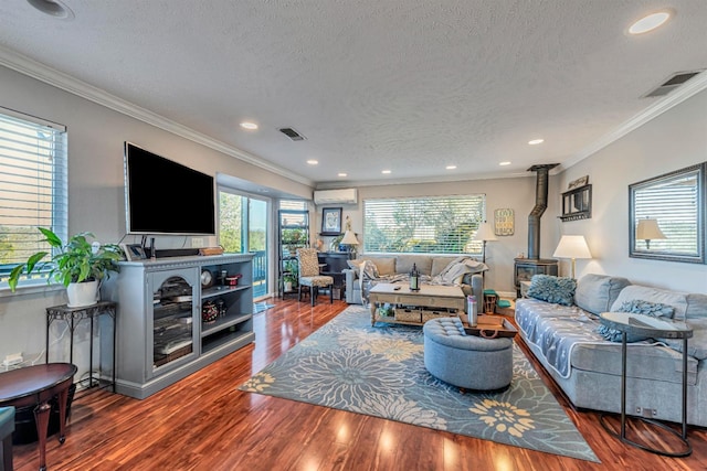 living room featuring ornamental molding, a wood stove, visible vents, and wood finished floors