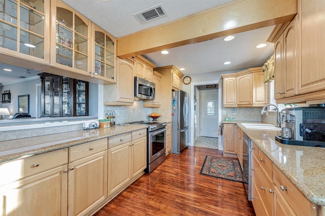 kitchen featuring stainless steel appliances, visible vents, light brown cabinetry, glass insert cabinets, and a sink