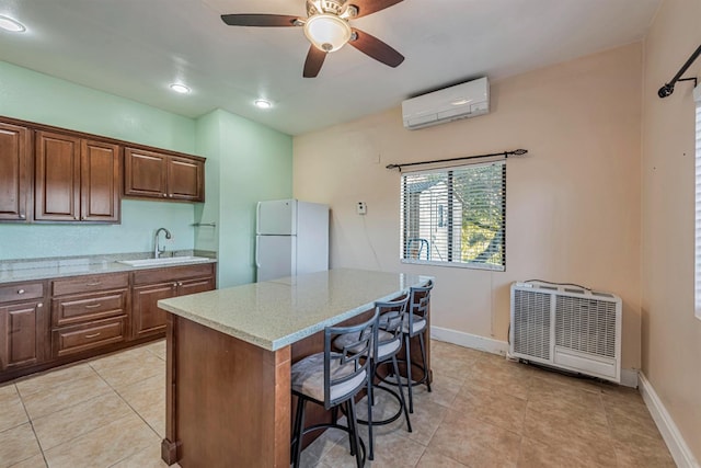 kitchen with freestanding refrigerator, an AC wall unit, a sink, light stone countertops, and a kitchen breakfast bar