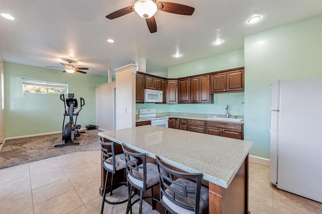 kitchen featuring a breakfast bar, light tile patterned floors, a kitchen island, a sink, and white appliances