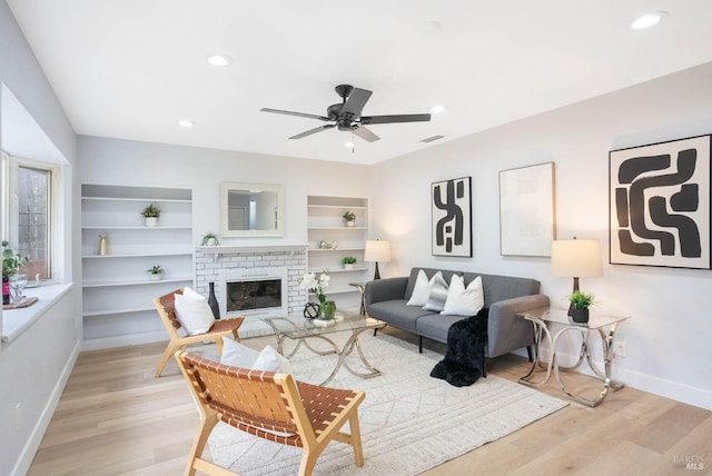 living room featuring a brick fireplace, ceiling fan, and light wood-type flooring