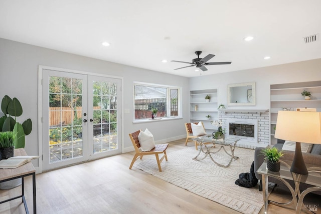 living room featuring light wood-type flooring, ceiling fan, french doors, a fireplace, and built in features