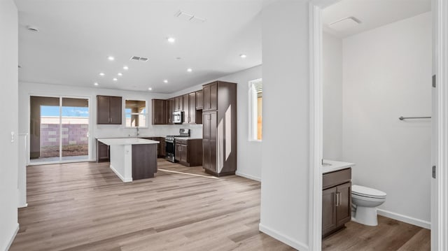 kitchen featuring a breakfast bar area, dark brown cabinets, a kitchen island, stainless steel appliances, and light hardwood / wood-style floors