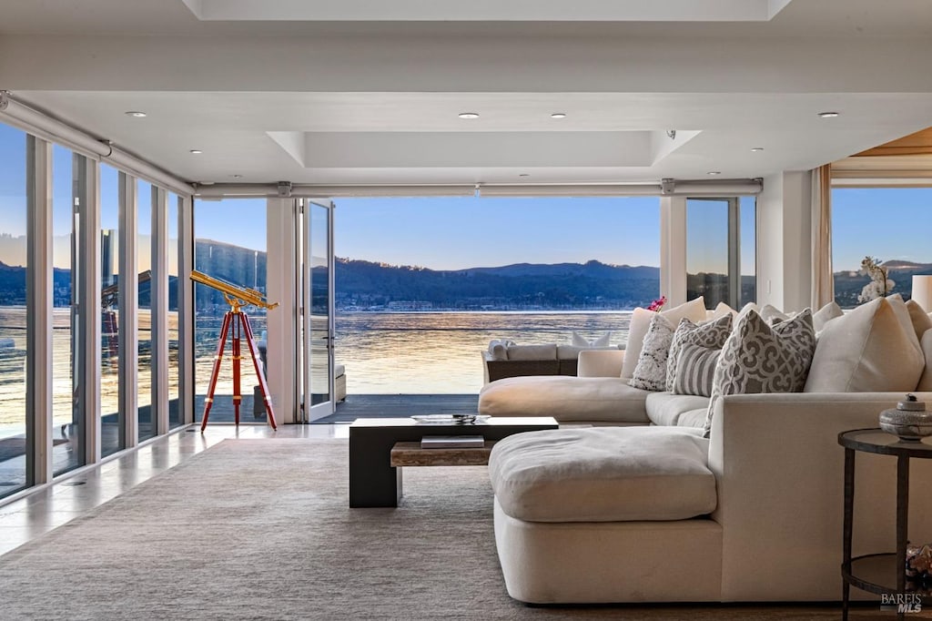 tiled living room featuring floor to ceiling windows, a water and mountain view, and a healthy amount of sunlight