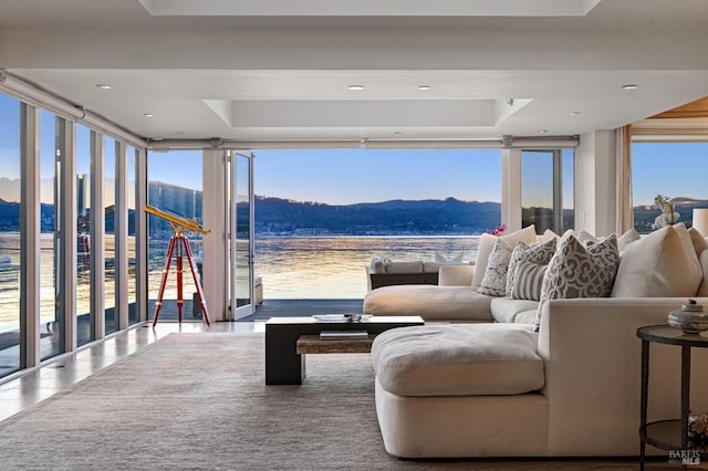 tiled living room featuring floor to ceiling windows, a water and mountain view, and a healthy amount of sunlight