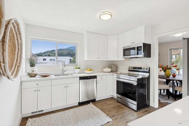 kitchen with sink, white cabinets, light wood-type flooring, and appliances with stainless steel finishes