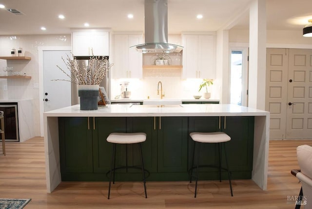 kitchen with a sink, island exhaust hood, white cabinetry, and light wood-style floors