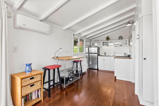 kitchen featuring lofted ceiling with beams, stainless steel fridge, dark hardwood / wood-style flooring, white cabinets, and a wall mounted air conditioner