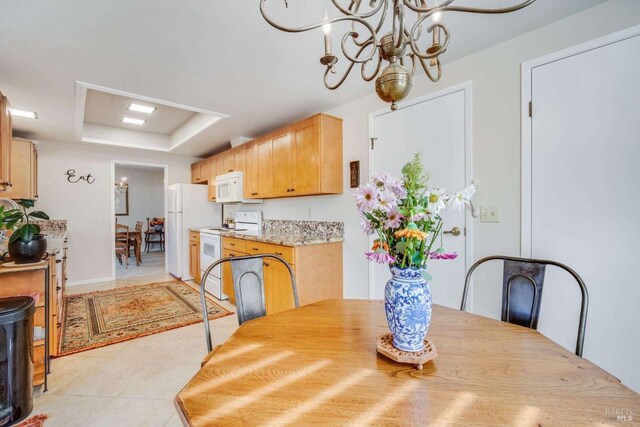 dining area with a tray ceiling, light tile patterned floors, and a chandelier