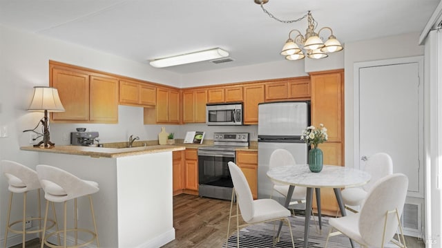 kitchen featuring a chandelier, stainless steel appliances, kitchen peninsula, dark wood-type flooring, and sink