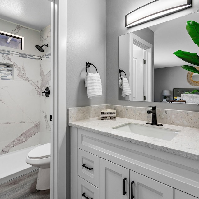 bathroom with a tile shower, vanity, hardwood / wood-style floors, and toilet