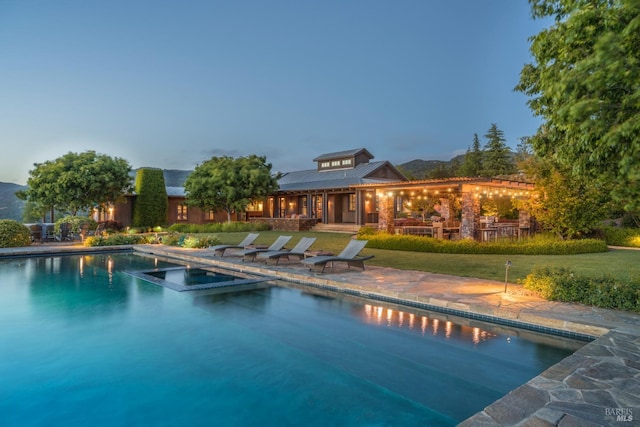 pool at dusk with a patio area, a lawn, and an in ground hot tub