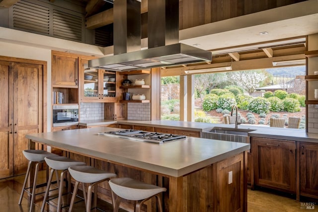 kitchen with island range hood, stainless steel gas cooktop, built in microwave, a breakfast bar, and backsplash