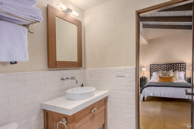 bathroom featuring a wainscoted wall, beam ceiling, tile walls, ensuite bathroom, and vanity