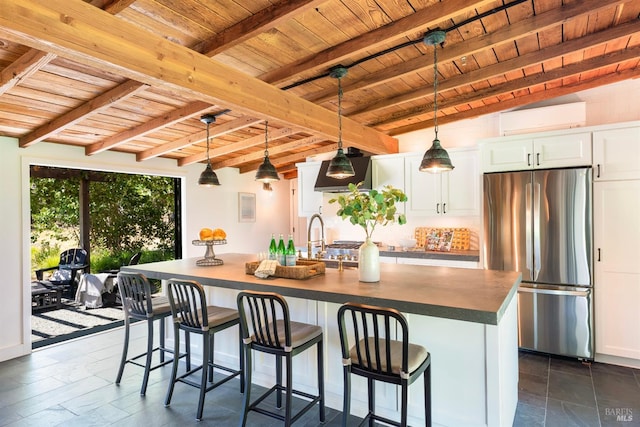 kitchen featuring an island with sink, beam ceiling, stainless steel fridge, and white cabinets