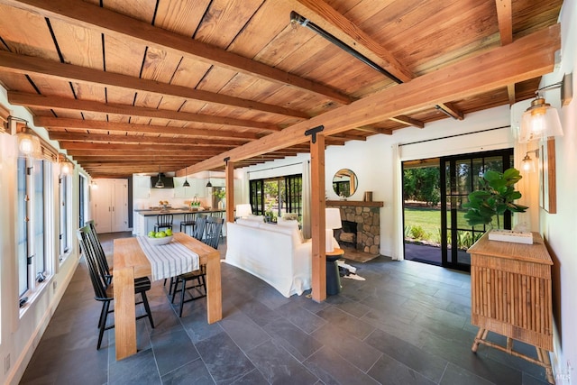 sunroom / solarium with beam ceiling, wood ceiling, and a stone fireplace