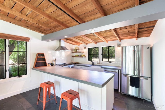 kitchen featuring wall chimney exhaust hood, kitchen peninsula, a breakfast bar area, wood ceiling, and appliances with stainless steel finishes