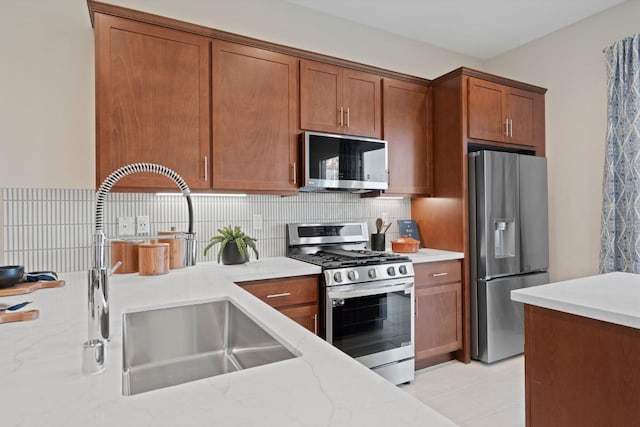 kitchen featuring tasteful backsplash, brown cabinets, light stone countertops, stainless steel appliances, and a sink