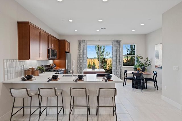 kitchen with a breakfast bar area, appliances with stainless steel finishes, backsplash, a peninsula, and a sink