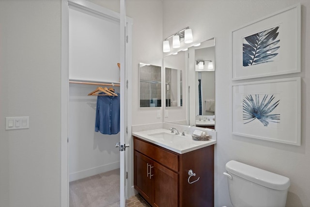 bathroom featuring baseboards, vanity, toilet, and a walk in closet