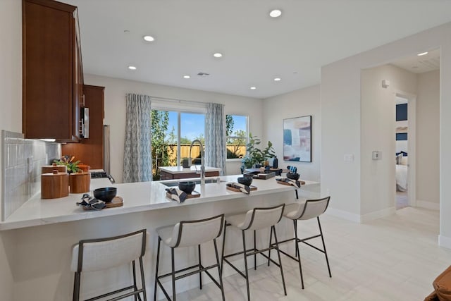 kitchen with a kitchen breakfast bar, backsplash, a peninsula, a sink, and recessed lighting