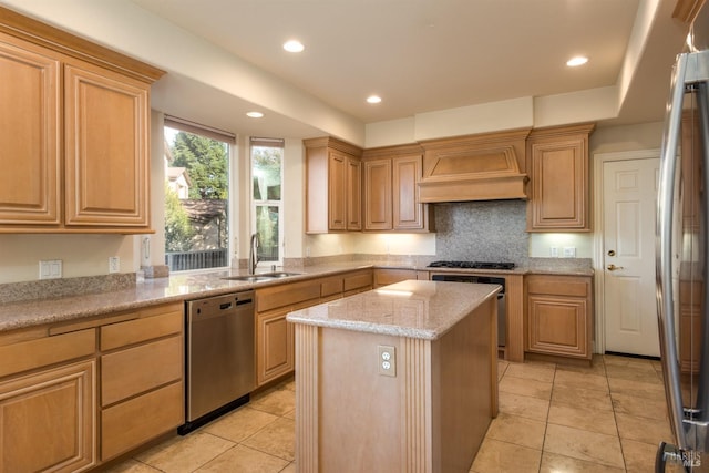 kitchen with light stone countertops, premium range hood, a sink, appliances with stainless steel finishes, and a center island
