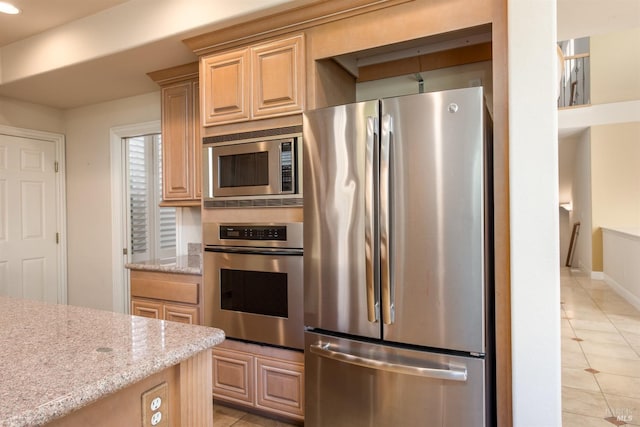 kitchen with light tile patterned floors, stainless steel appliances, light stone counters, and light brown cabinetry