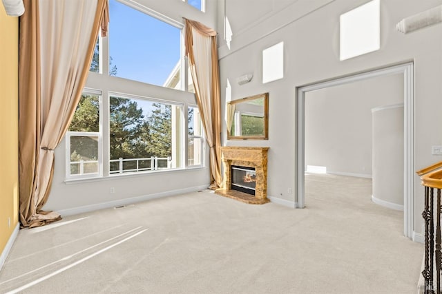 unfurnished living room featuring baseboards, visible vents, carpet floors, a high ceiling, and a glass covered fireplace