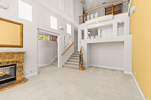 carpeted living room featuring visible vents, baseboards, a high ceiling, a fireplace, and stairs